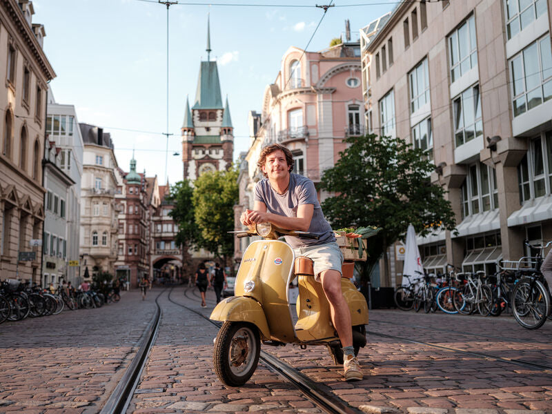 Ben Kindler auf einer gelben Vespa in der Freiburger Altstadt