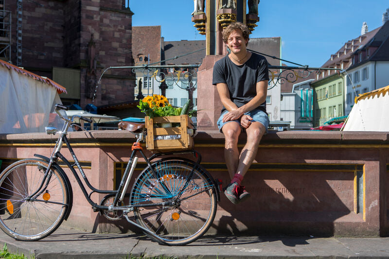 Ben Kindler sitzt auf dem Rand eines Brunnens mit einem angelehnten Fahrrad